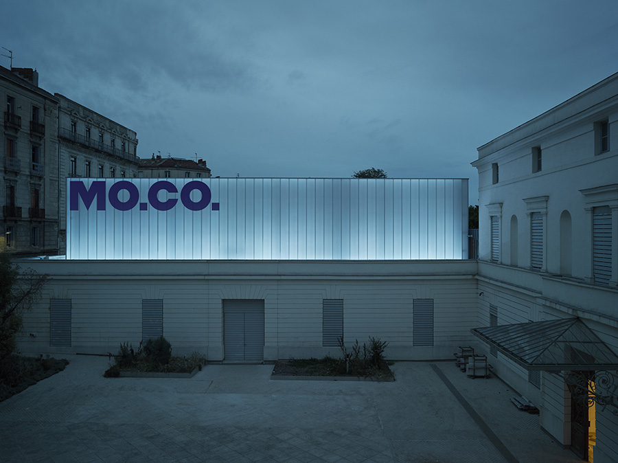 A museum with the words 'MO.CO.' on its glassed facade.