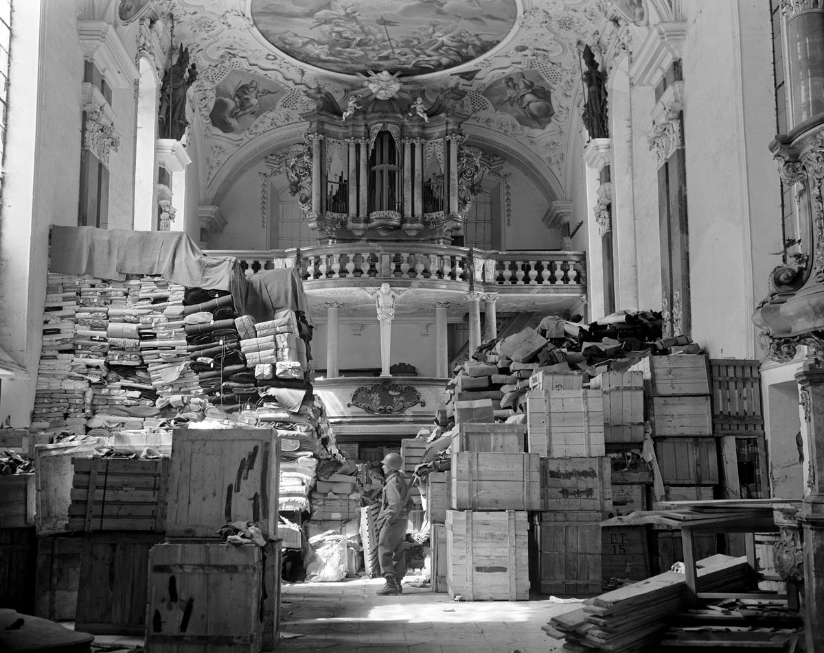 Archival photograph of Nazi-looted art in various crates and piles of paintings wrapped and stacked in a church.