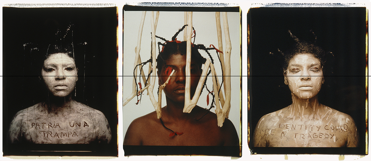 A triptych of Polaroid portraits of a black person. In the left and right image, they are covered in white paint, with a phrase carved into the paint's surface on their chest. On the right, their chest reads "patria una trampa." On the right, it reads "identity could be a tragedy." In the middle, they appear surrounded by a cage-like structure made of what looks like sticks or perhaps bones.