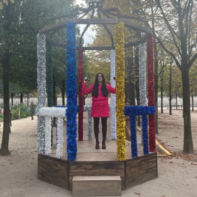 A woman in a pink dress stands in the middle of a bandstand decorated with multicolored tinsels.