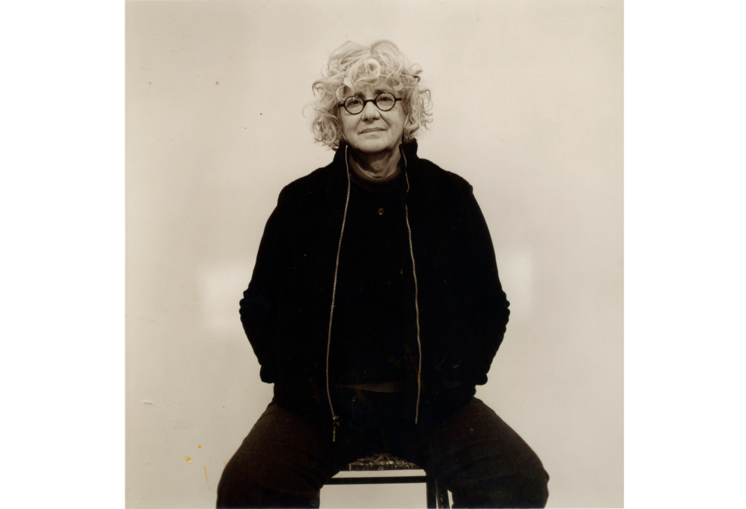 portrait of a woman with thick curly hair dressed in black and sitting in a chair.